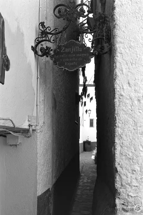 A black-and-white photo of looking along Calle Zanjilla with shear house walls on both sides, making the street look even narrower.