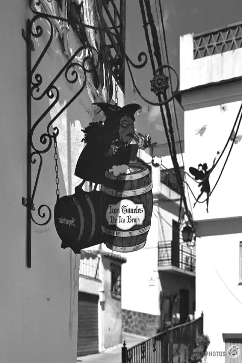 A black-and-white photo of a narrow street in Soportújar with a bar sign 'The Witch's Barrel'.