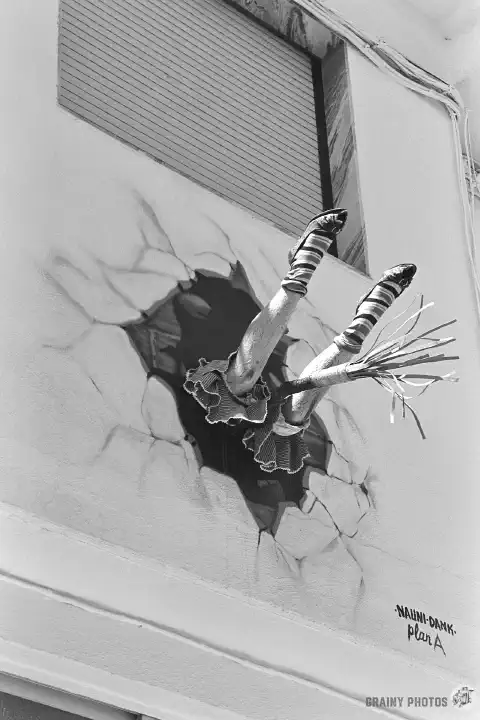 A black-and-white photo of a witch who crashed into the wall and got stuck in it. Only her legs and part of her broom are sticking out of the wall.