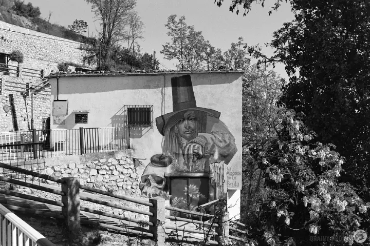 A black-and-white photo of a mural on a house wall of a witch casting a spell.