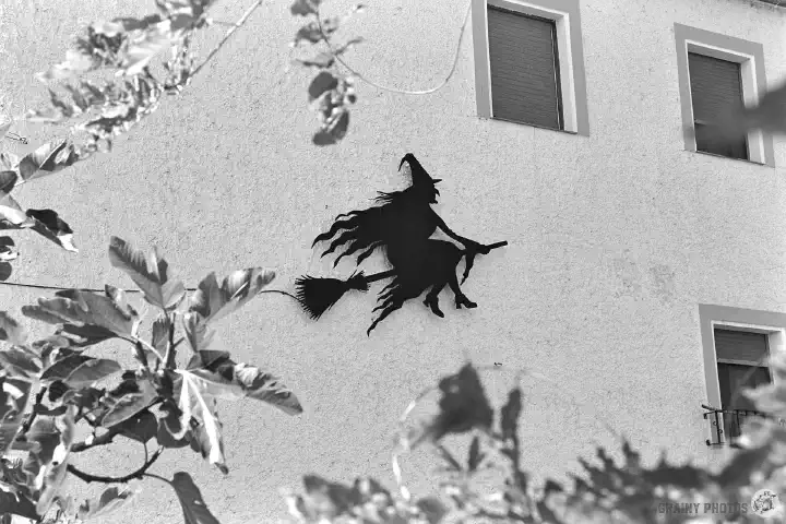 A black-and-white photo of the silhouette of a witch on a broom on the wall of a residential block.