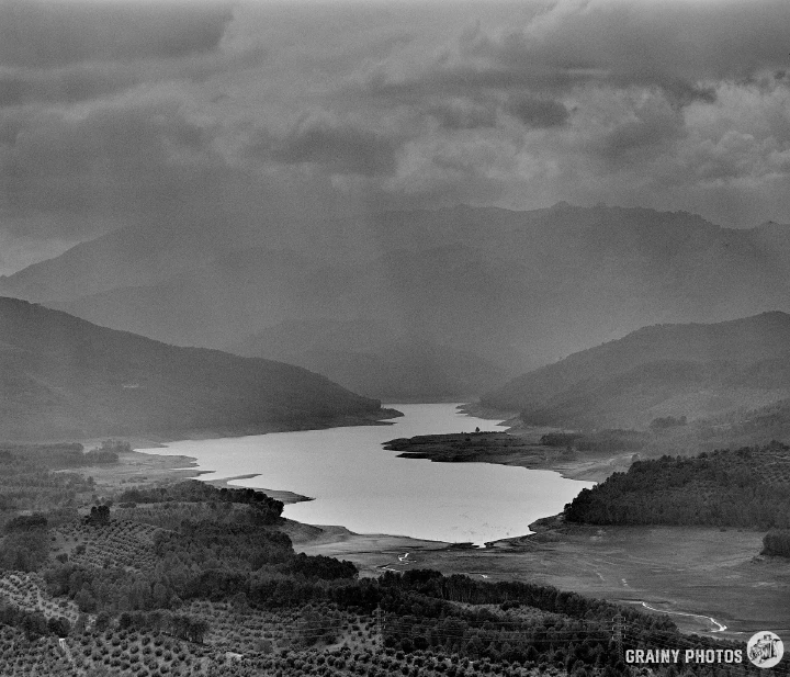 A black-and-white photo of Tranco reservoir with dark threatening clouds overhead.
