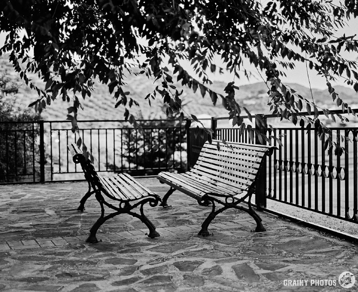 A black-and-white photo of two benches facing each other on a viewing terrace by a reservoir.
