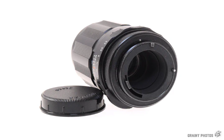 A photo of the Super-Takumar 135mm lens lying on its side with the threaded camera end foremost.