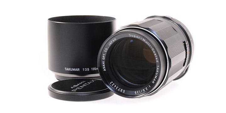 A photo of the Super-Takumar 135mm f3.5 lens with a lens hood and lens cap next to it.