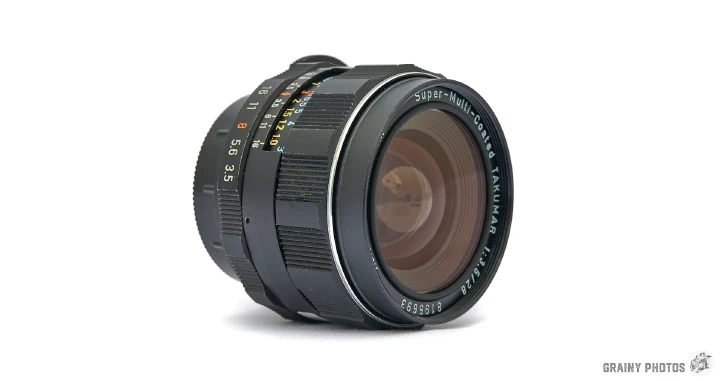 A photo of the Super-Takumar 28mm f3.5 lens lying on its side.