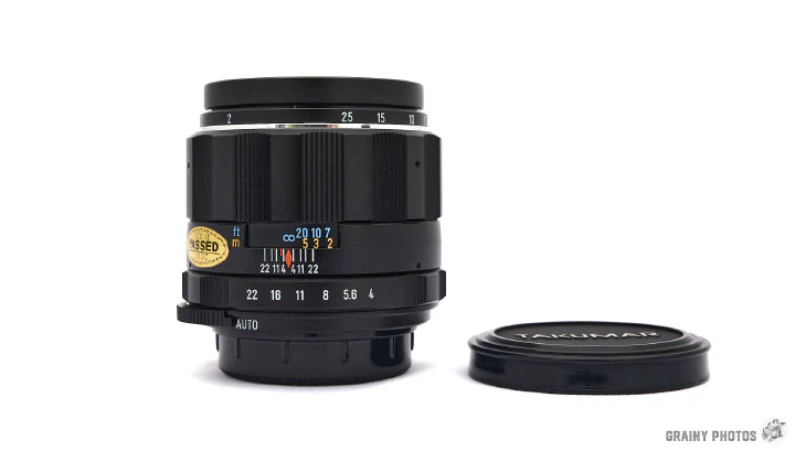 A photo of the Super-Multi-Coated Macro Takumar 50mm f4 lens standing on its end with a lens cap lying next to it.