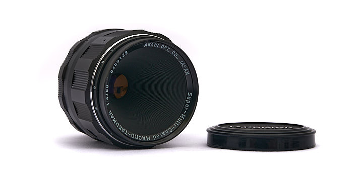 Photo of the Super-Multi-Coated Macro Takumar 50mm f4 lens with lens cap lying beside it.