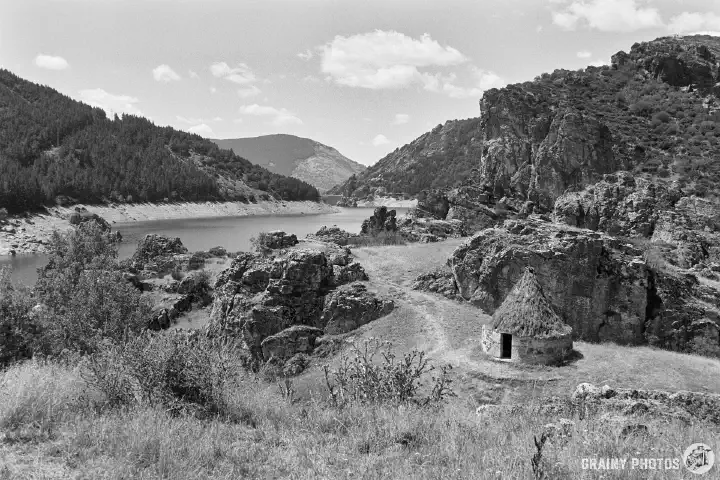 A black-and-white film photo of an old shepherd’s hut by the Camporredondo reservoir