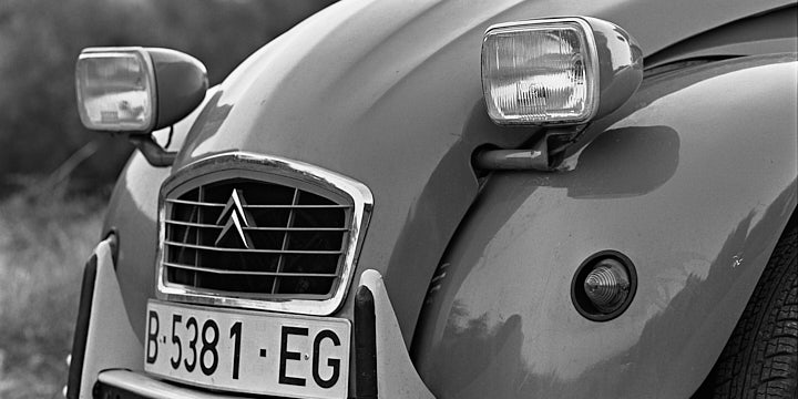 A black-and-white film photo of the front of a Citreon 2CV, concentrating mostly on the headlights and grill.