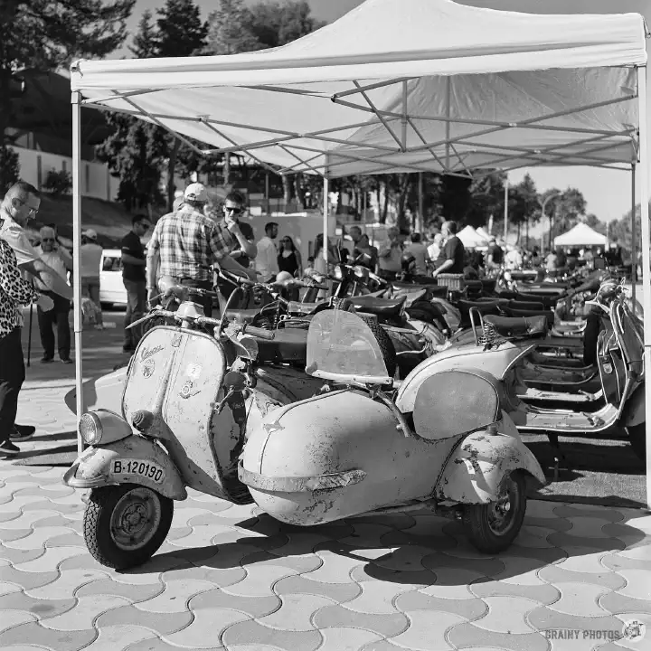 Black-and-white film photo of a row of scooters at the classic car show.