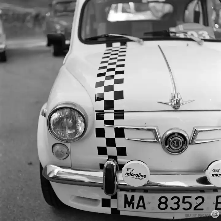 Black-and-white film photo of a Seat 600 with a checkered black and white stripe along the bonnet.