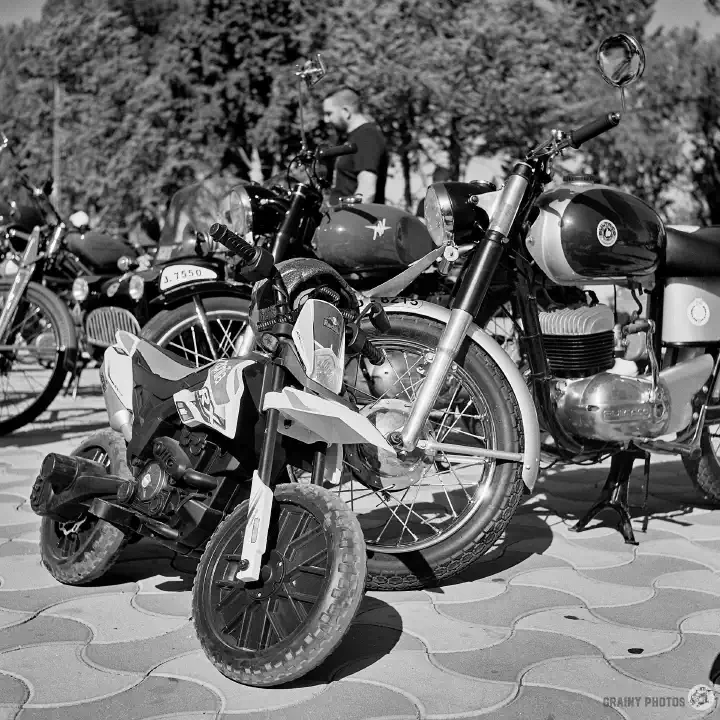 Black-and-white film photo of a motorbike and a small child's motorbike leaning against it.