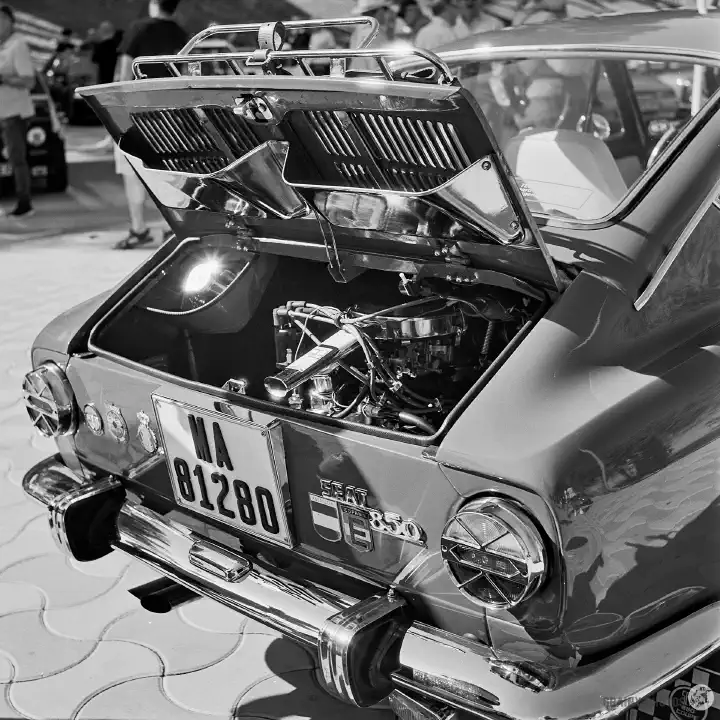 Black and white film photo of a Seat 850 with his rear engine cover open exposing the engine