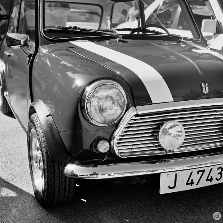 Black-and-white film photo of the front of a Mini. The car has a white stripe along the bonnet.