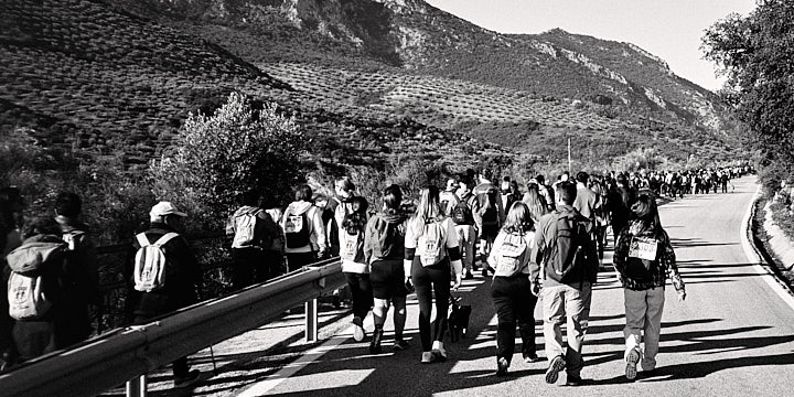 A black-and-white film photo of hikers walking on a path and road shortly after the start of the Cross Pantano del Víboras walking category