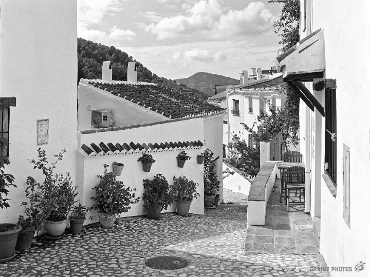 A black-and-white film photo of a cobbled street in the village