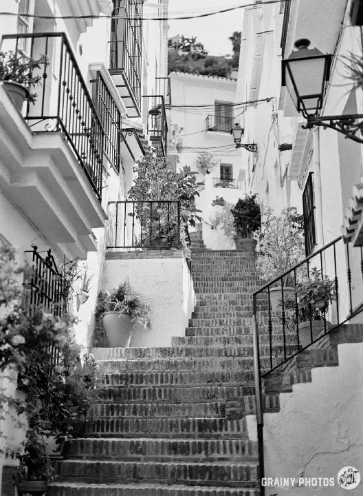 A black-and-white photo of steep steps meandering up between terraced white houses