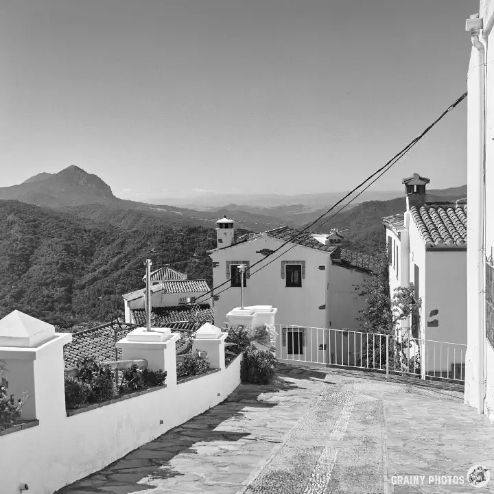 A black-and-white photo of a small, pretty terrace amongst several white houses. A mountain is visible in the distance.