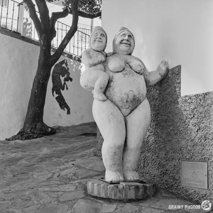 A black-and-white photo of a stone sculpture of a naked woman holding a baby.