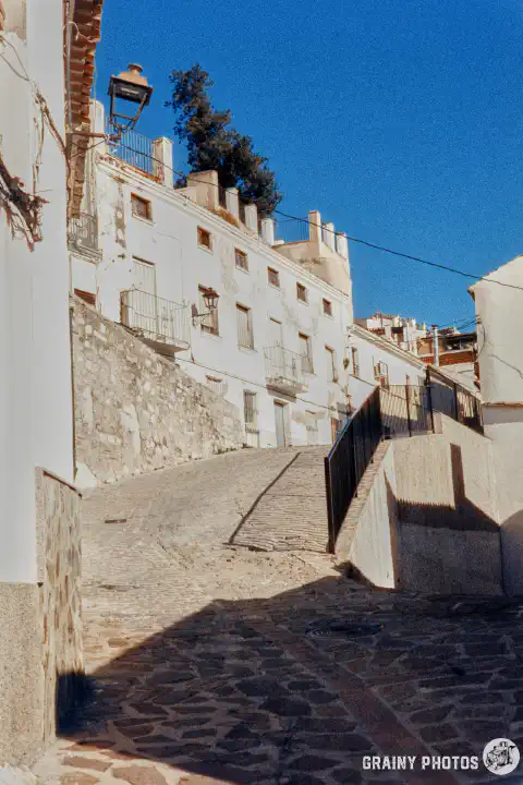 A colour film photo shot on Harman Phoenix 200 film. A cobbled street leading up to a row of white terraced townhouses.