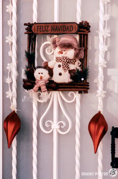 A colour film photo of Christmas decorations on a front door with the message Feliz Navidad.