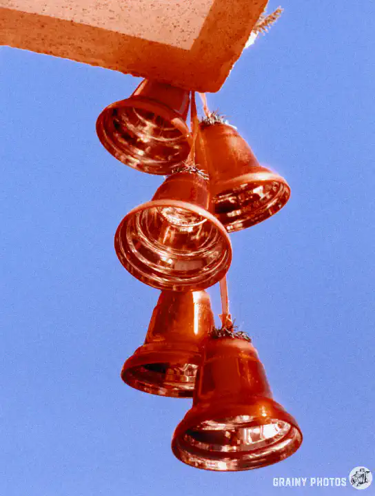 A colour film photo of red Christmas bell decorations against a blue sky.