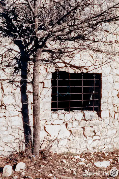 A colour film photo of a window opening with metal reinforcing mesh in a stone building used for storage.