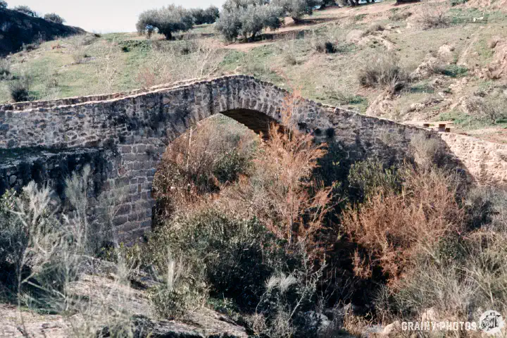 A colour film photo of a stone arched Roman bridge