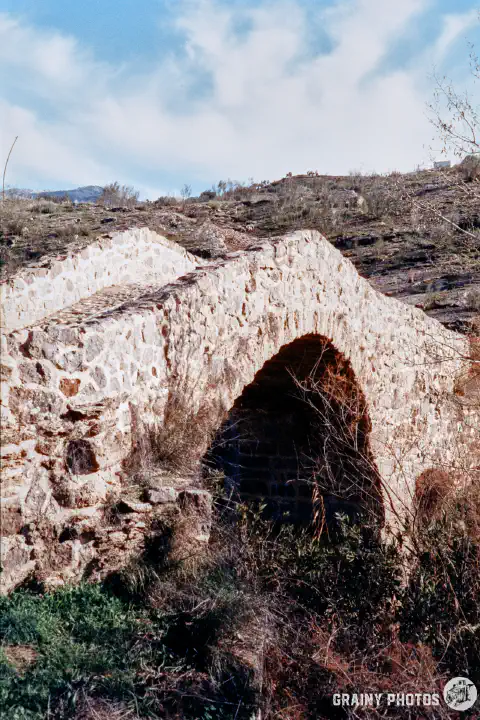 A colour film photo of a stone arched Roman bridge