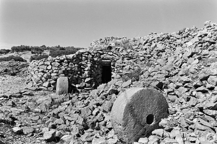 Black-and-white photo of two millstones by the entrance to a stonemason's hut.