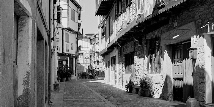 A black-and-white film photo of a narrow street in Mogarraz
