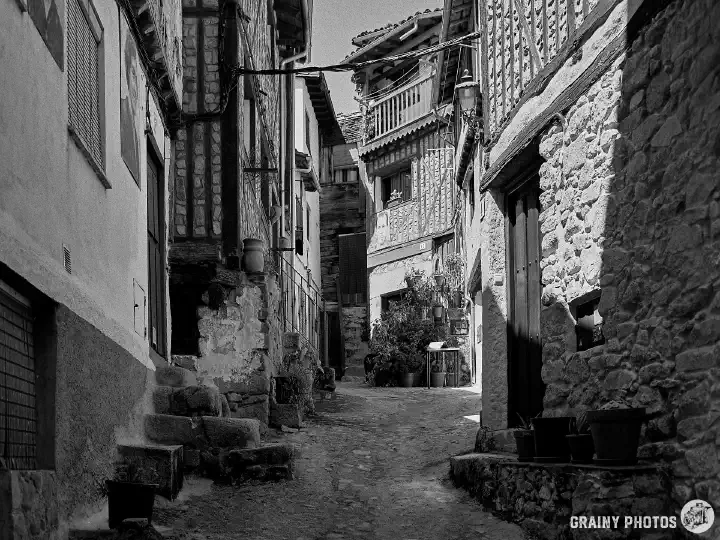 A black-and-white film photo of a blind, side alley with old stone and timber-framed houses.