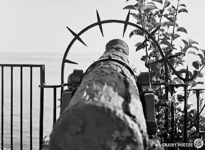 A black and white film photo looking along an old canon pointing out to sea.