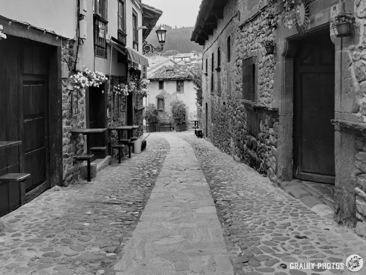 A black-and-white film photo of a cobbled street in the old part of Potes with pretty stone houses on both sides.