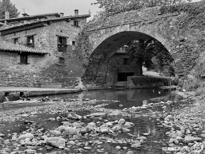 A black-and-white film photo of San Cayetano bridge with a stoney river bed and river flowing under.