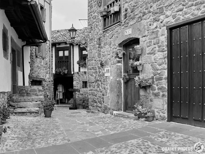 A black-and-white film photo of a small courtyard-style area between old houses. At the far end is an open door into an arts and crafts store.