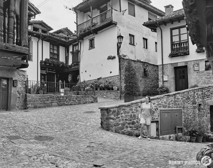 A black-and-white film photo of a cobbled street zig-zagging its way up a hill between stone houses, some with timber balconies.