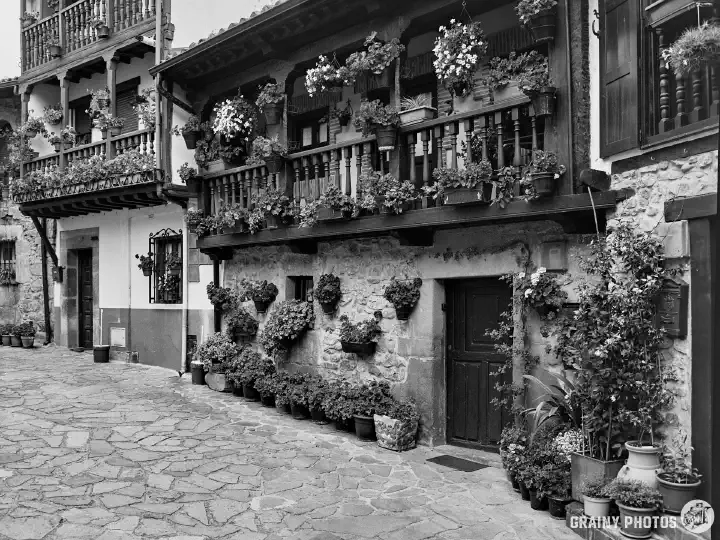 A black-and-white film photo of old traditional stone houses utilising structural timber and wooden balconies.