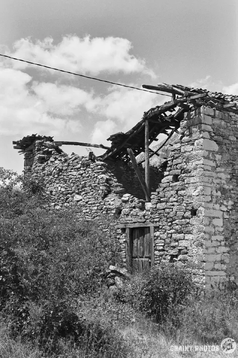 A black-and-white film photo of the collapsed roof on one of the abandoned houses