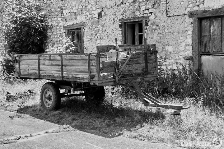 A black-and-white film photo of an abandoned trailer outside one of the houses