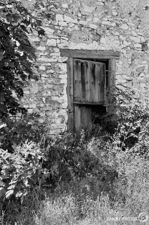 A black-and-white film photo of an old barn door on one of the abandoned houses