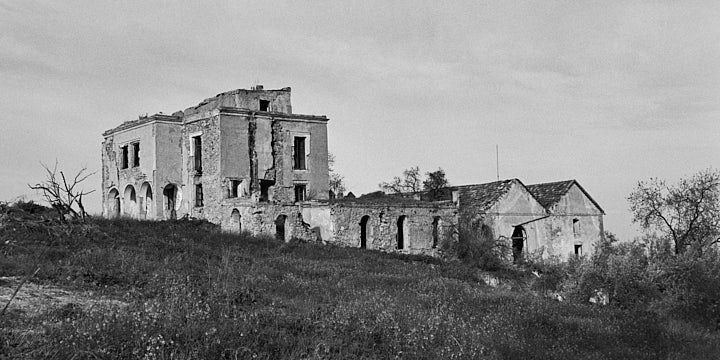 A black-and-white film photo of a very grand abandoned cortijo complex. The main house is on the left with various outbuildings to the right.