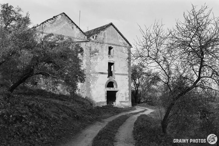 A black-and-white photo looking along a dirt track at the side of the cortijo outbuildings.