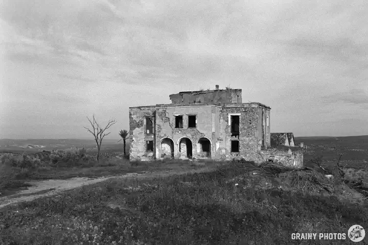 A black-and-white photo of an abandoned cortijo set in a flat landscape.
