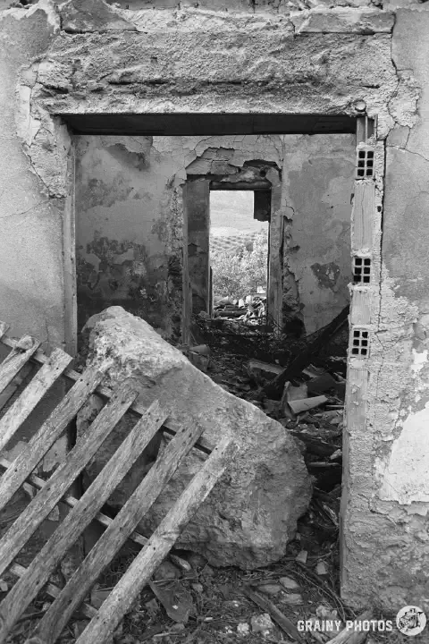 A black-and-white photo looking into the cortijo through the front door. The doorway is blocked by a large boulder and pallet. You can see right through the property through an internal door opening and out through the back door. There are no doors.