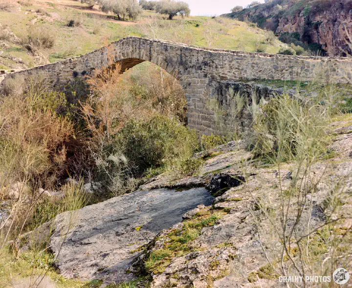 A colour film photo of a stone arched bridge dating back to Roman times, across the Viboras river.