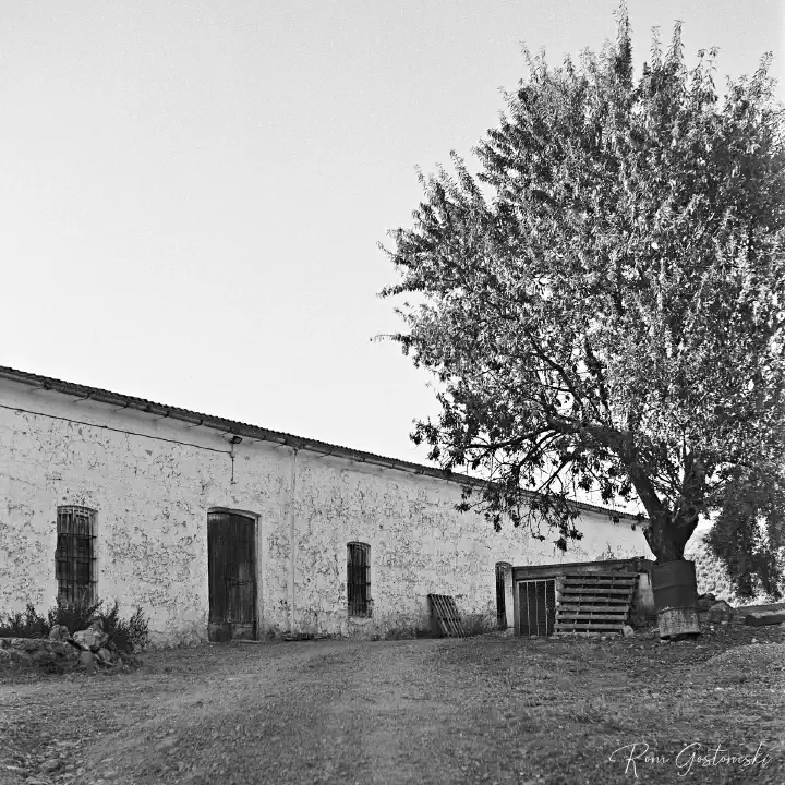 A black-and-white film photo of low outbuildings to the side of the cortijo