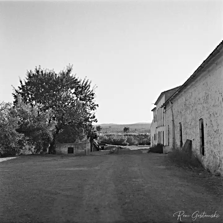 A black-and-white film photo looking along the building line with outbuildings and the cortijo in the distance.