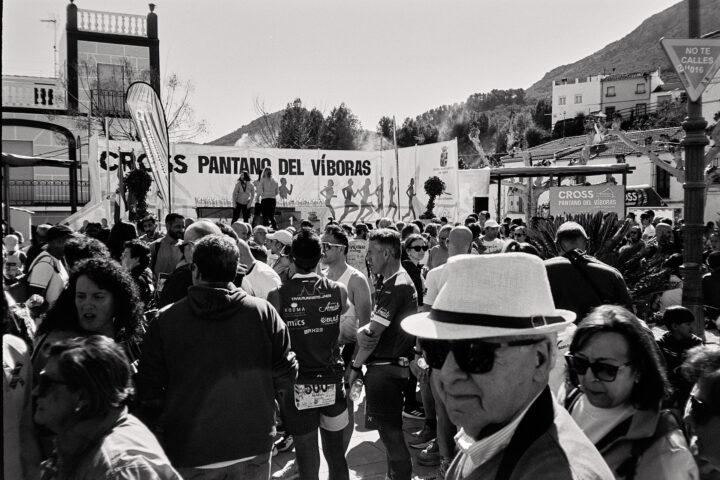 A crowded event scene after the Pantano del Víboras, featuring participants in sports gear, spectators, and banners promoting the cross event. The atmosphere is lively, with people gathered in a sunny setting.